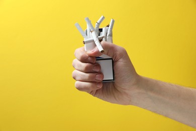 Stop smoking. Man holding pack with broken cigarettes on yellow background, closeup