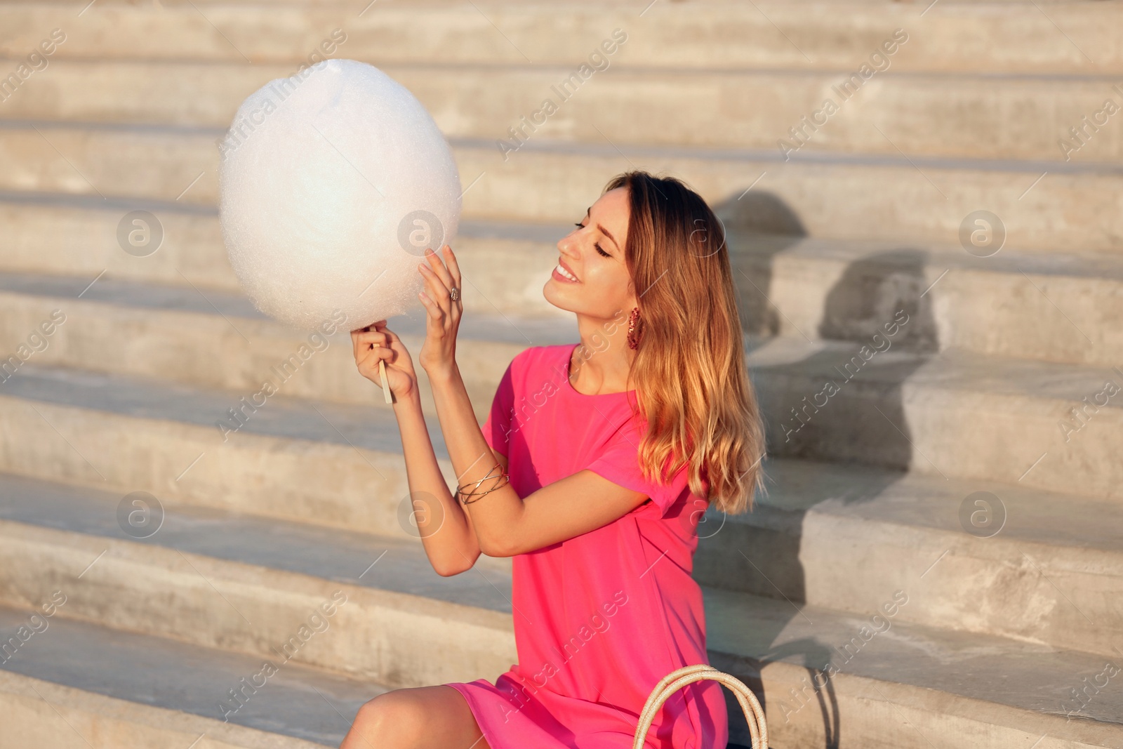 Photo of Happy young woman with cotton candy on stone stairs