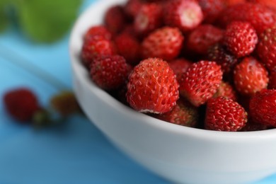 Fresh wild strawberries in bowl on light blue table, closeup