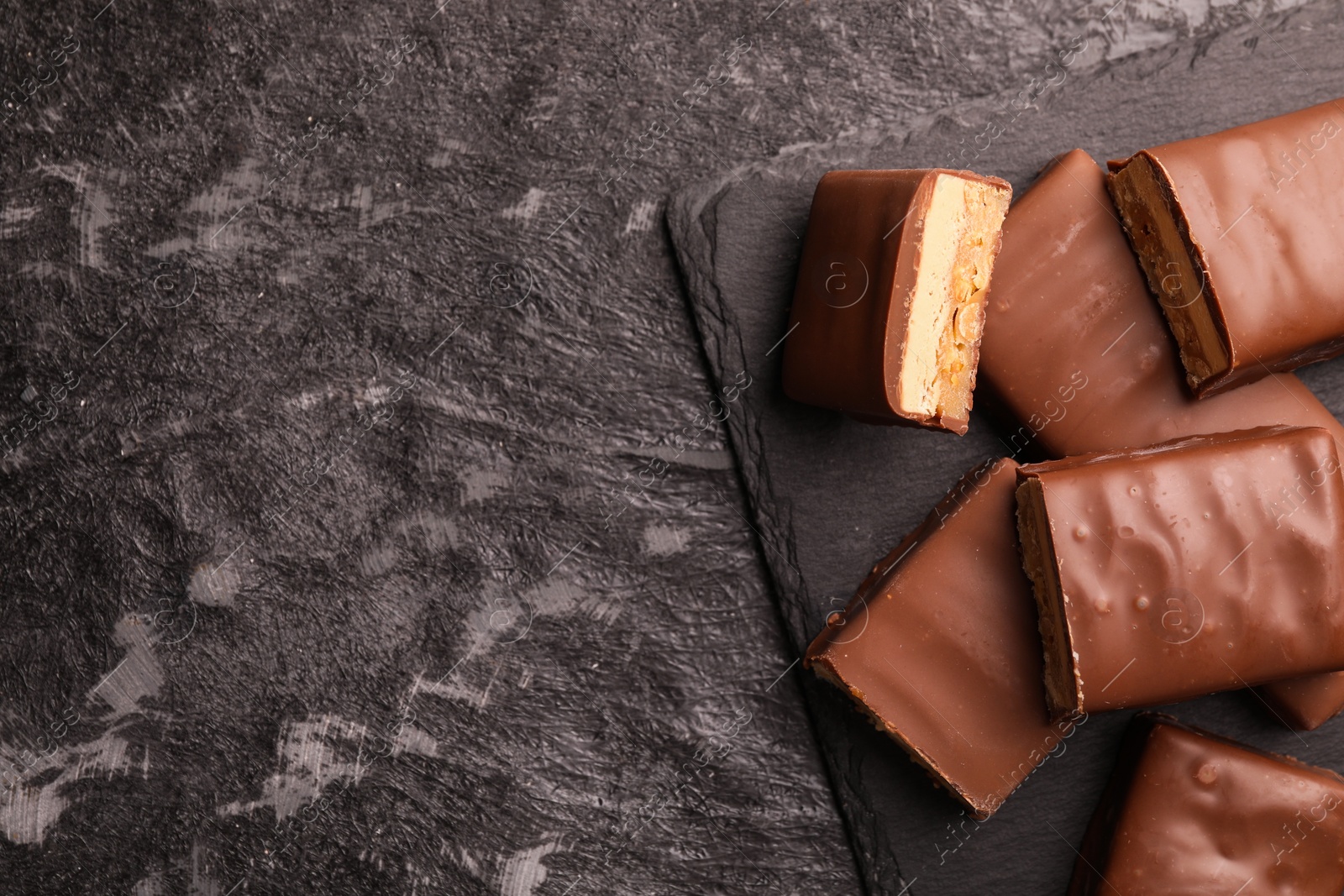 Photo of Tasty chocolate bars with nougat on gray textured table, top view. Space for text