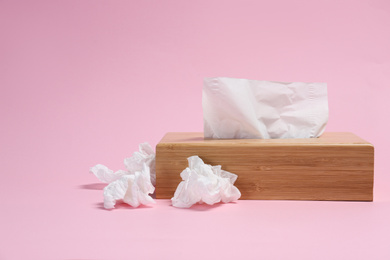 Photo of Holder with paper tissues and used crumpled napkins on pink background