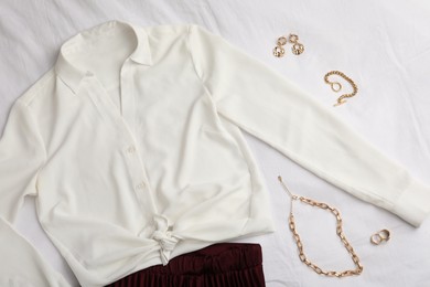 Photo of Stylish clothes and golden bijouterie on white fabric, flat lay