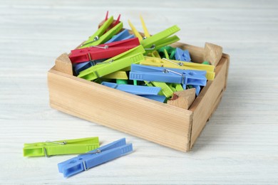 Crate with colorful clothespins on white wooden table