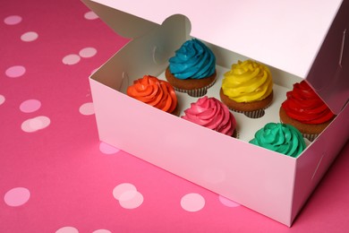 Box with different cupcakes and confetti on pink background