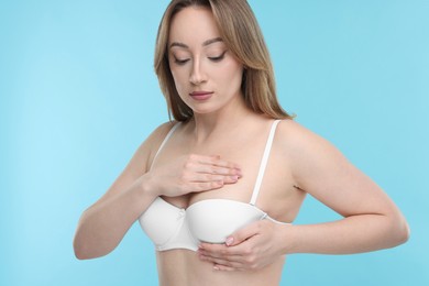 Photo of Mammology. Young woman doing breast self-examination on light blue background