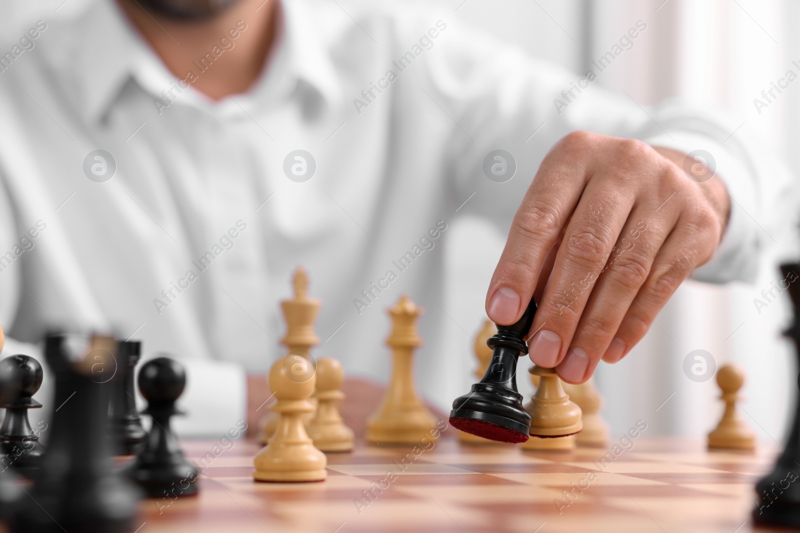 Photo of Man moving chess pieces at checkerboard indoors, closeup