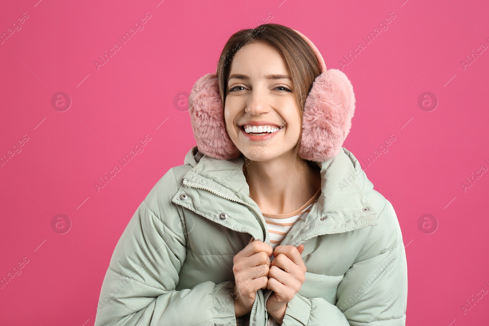 Photo of Happy woman wearing warm earmuffs on pink background