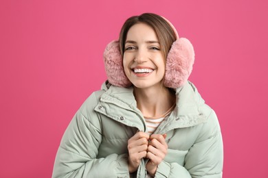 Happy woman wearing warm earmuffs on pink background