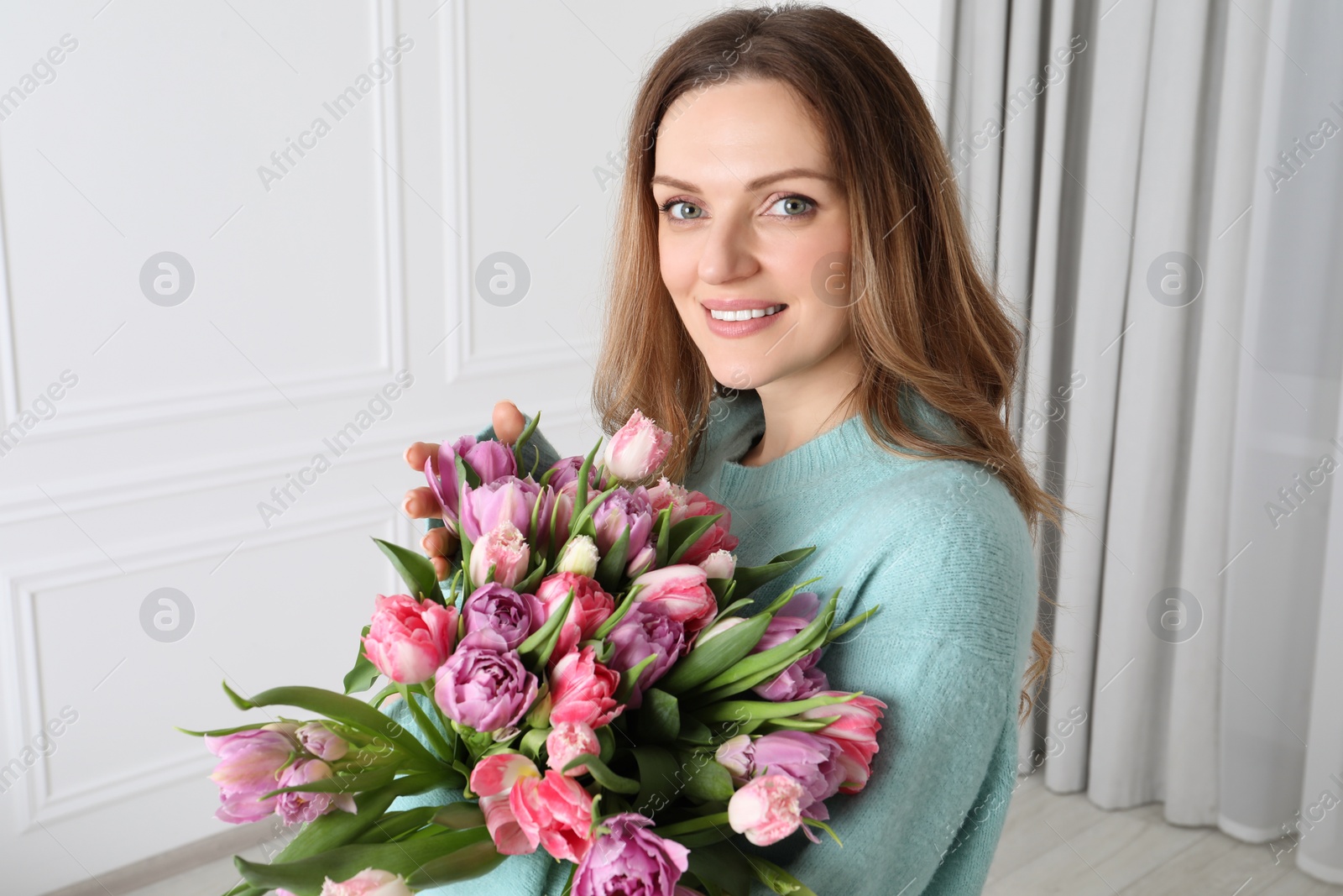 Photo of Happy young woman with bouquet of beautiful tulips indoors