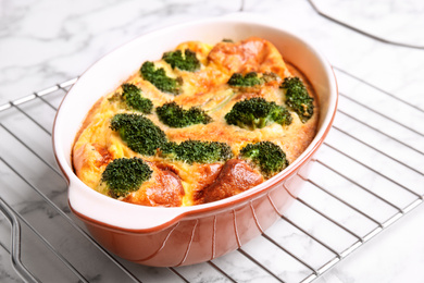 Photo of Tasty broccoli casserole in baking dish on cooling rack, closeup