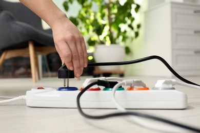 Woman inserting power plug into extension cord on floor indoors, closeup. Electrician's professional equipment