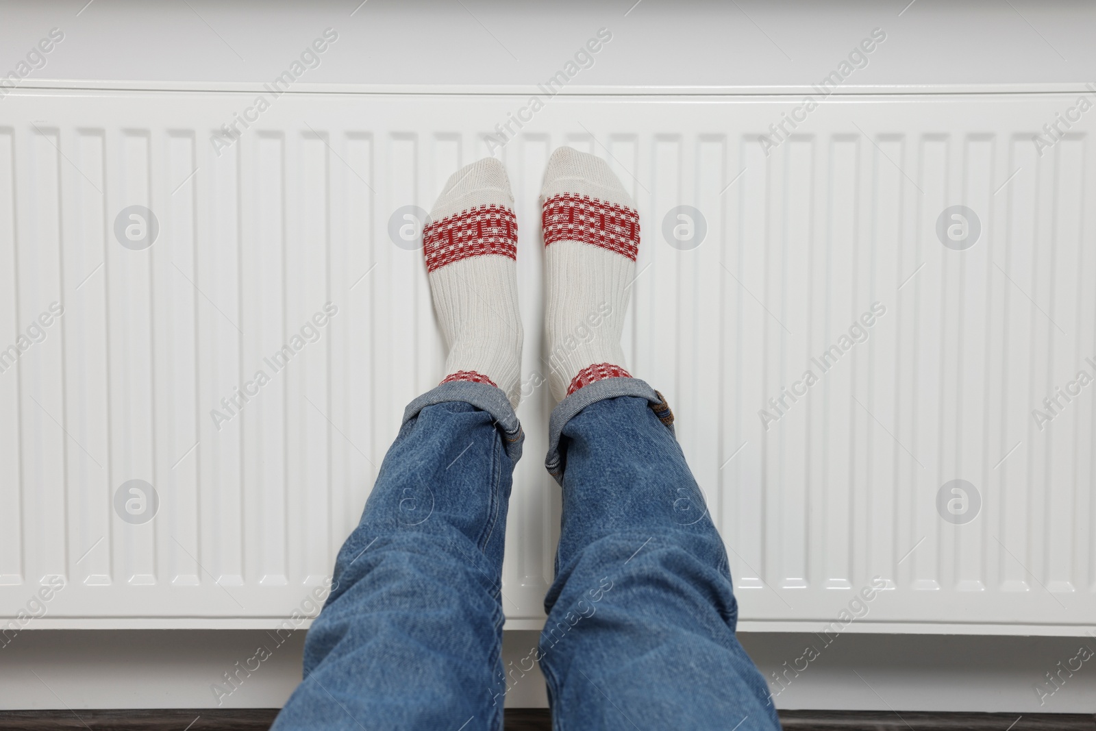 Photo of Woman warming legs on heating radiator near white wall, closeup