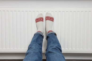 Woman warming legs on heating radiator near white wall, closeup