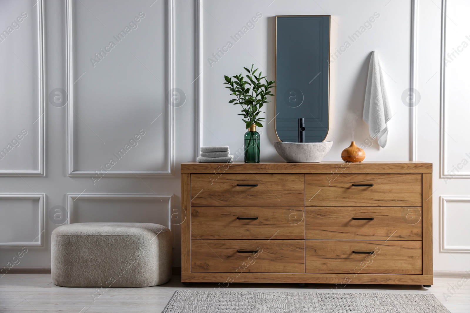 Photo of Modern bathroom interior with stylish mirror, eucalyptus branches, wooden vanity and pouf