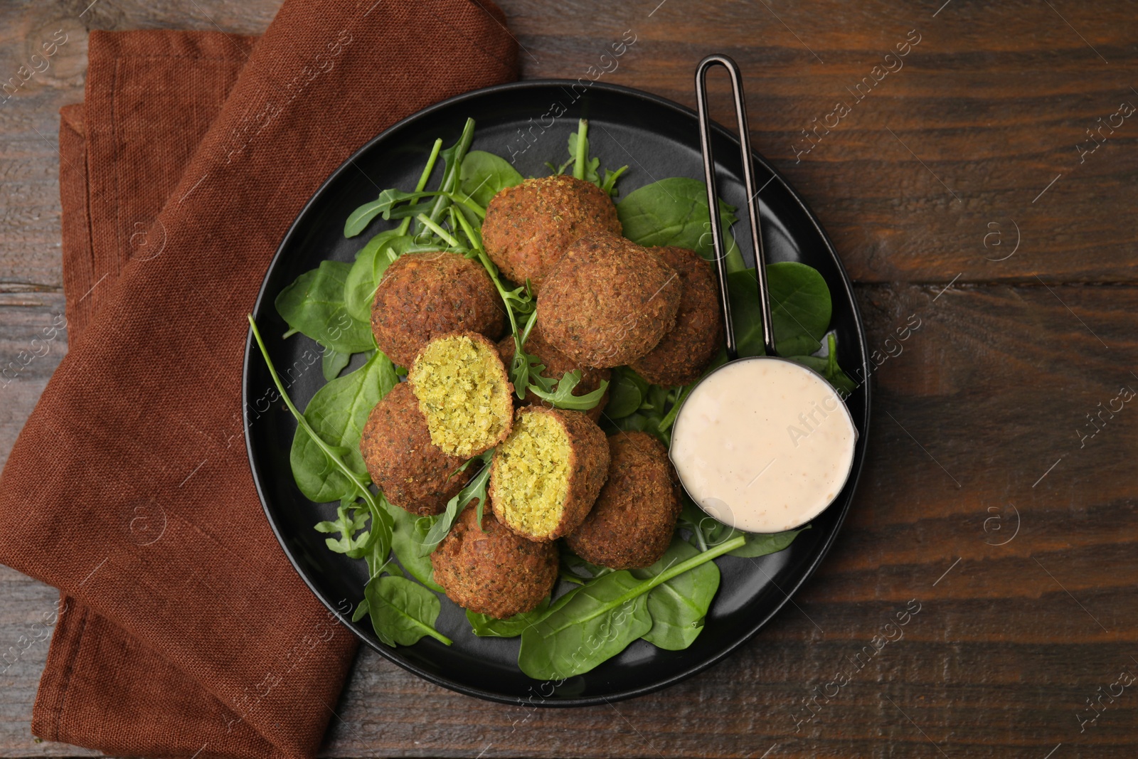 Photo of Delicious falafel balls, herbs and sauce on wooden table, top view