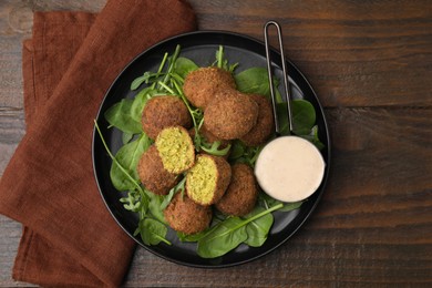 Photo of Delicious falafel balls, herbs and sauce on wooden table, top view