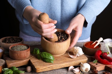 Photo of Woman grinding peppercorns at wooden table, closeup