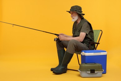 Fisherman with fishing rod on chair against yellow background