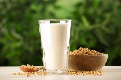 Glass with fresh soy milk and grains on white wooden table against blurred background