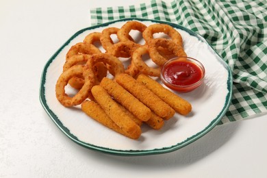 Photo of Plate with tasty ketchup, cheese sticks and onion rings on white table, closeup