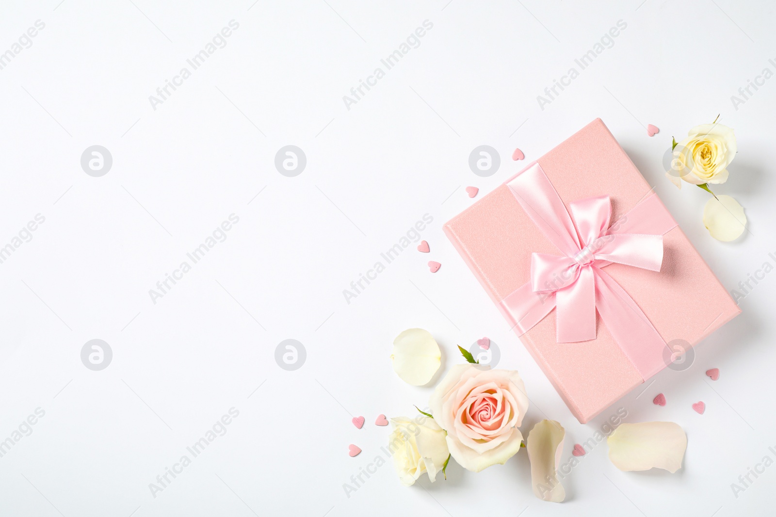 Photo of Pink gift box and beautiful flowers on white background, flat lay. Space for text
