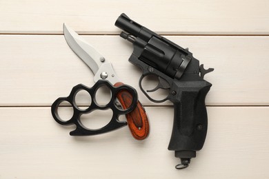 Photo of Black brass knuckles, gun and knife on white wooden background, flat lay