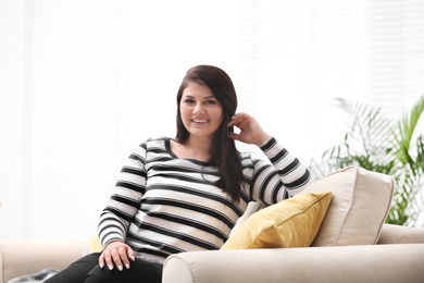 Beautiful overweight woman on sofa in living room. Plus size model