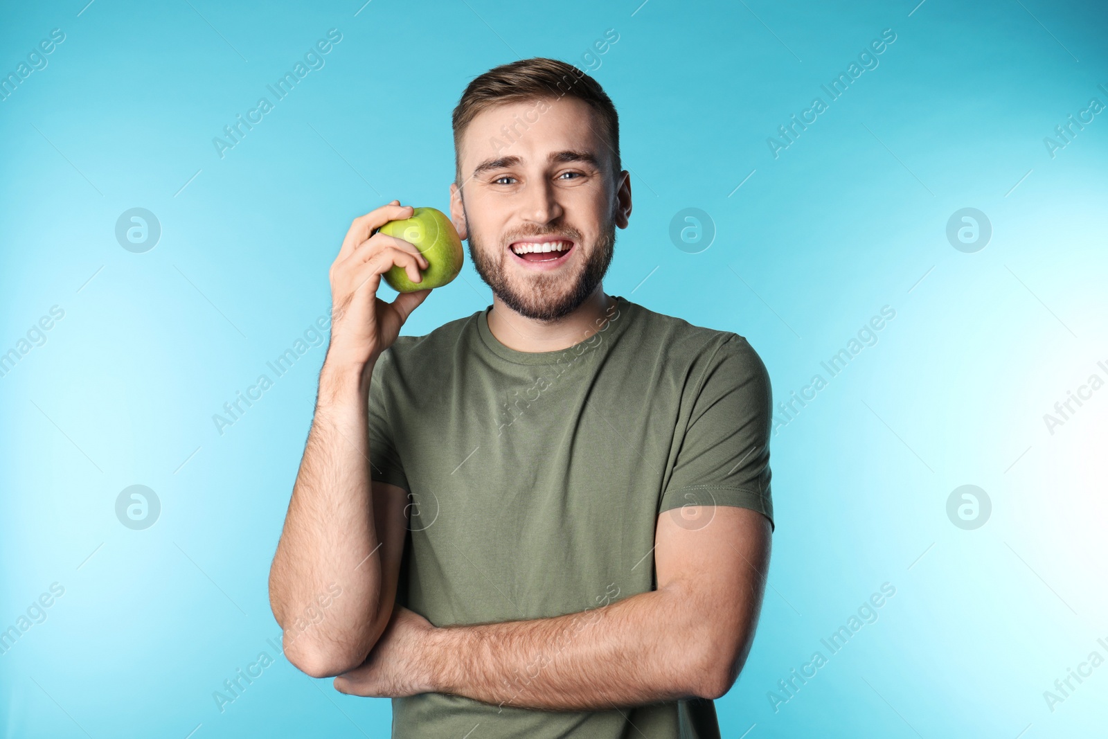 Photo of Young man with healthy teeth and apple on color background