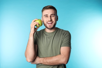 Young man with healthy teeth and apple on color background