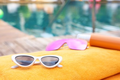 Sunglasses and sunscreen on beach towel near outdoor swimming pool at luxury resort, closeup. Space for text