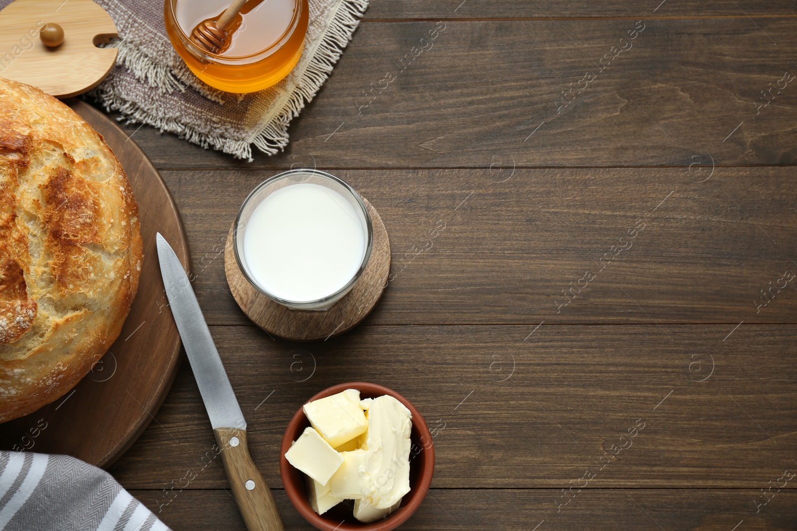 Photo of Glass with fresh milk, honey, butter and bread on wooden table, flat lay. Space for text