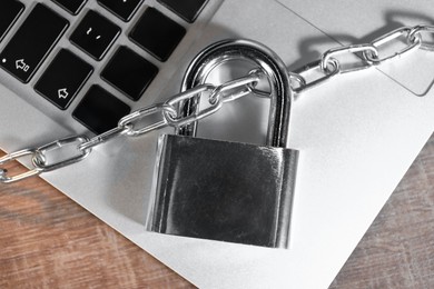 Photo of Cyber security. Laptop with padlock and chain on wooden table, top view