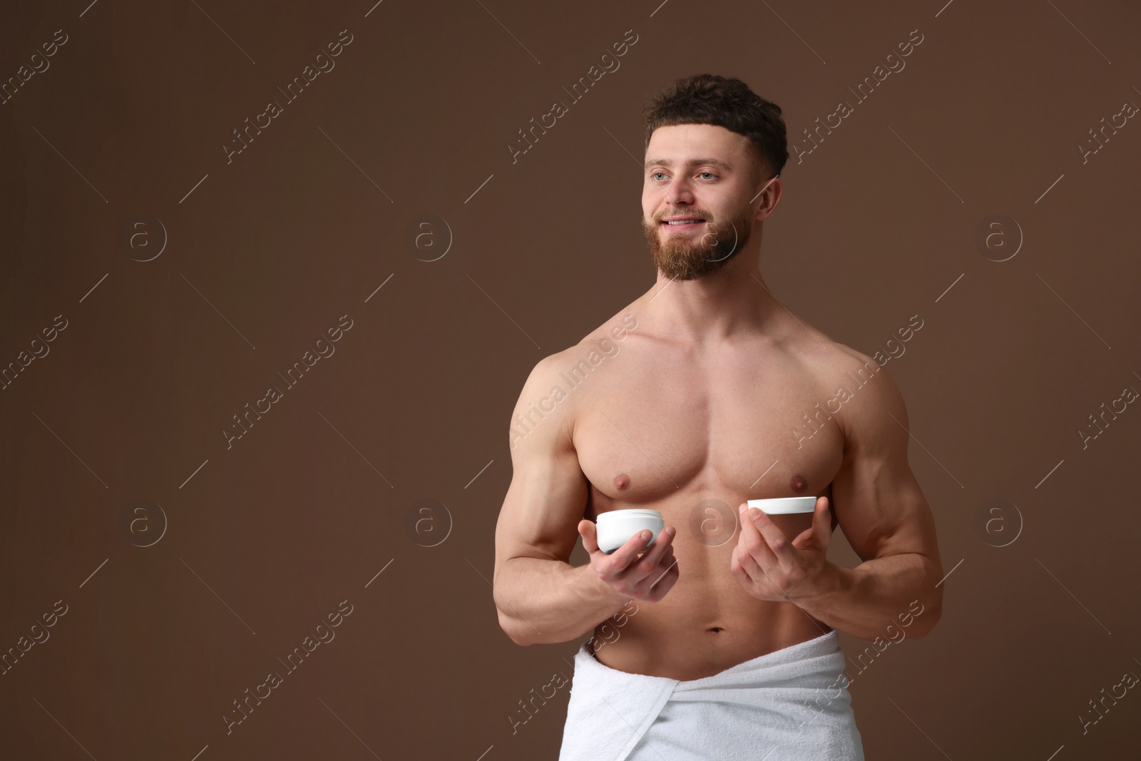 Photo of Handsome man holding jar with moisturizing cream on brown background, space for text