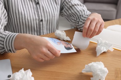 Woman ripping photo near paper napkins at wooden table indoors, closeup. Divorce concept