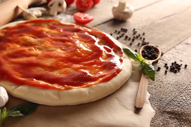 Photo of Pizza dough smeared with tomato sauce and products on wooden table, closeup