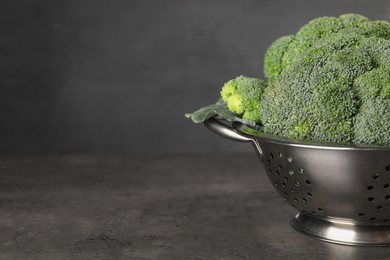 Colander with fresh raw broccoli on grey table, closeup. Space for text