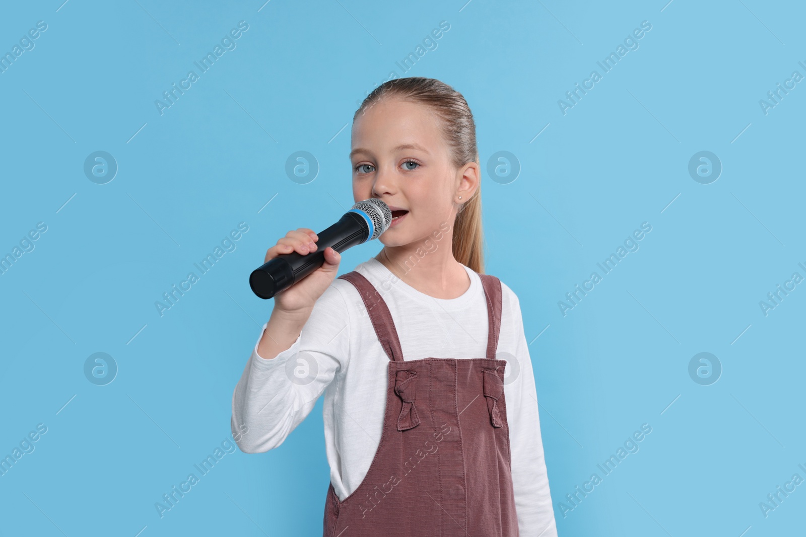 Photo of Cute little girl with microphone singing on light blue background