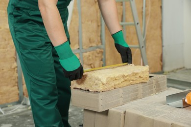 Photo of Worker measuring thermal insulation material indoors, closeup