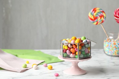 Delicious colorful dragee candies on white marble table, space for text