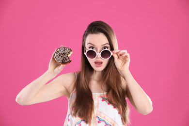 Photo of Beautiful young woman wearing sunglasses with donut on pink background