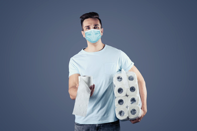 Image of Man in medical mask holding toilet paper rolls on grey background