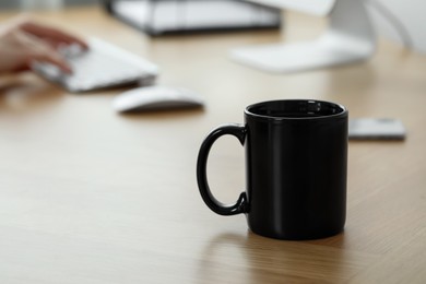 Photo of Black ceramic mug on wooden table in office, selective focus. Space for text