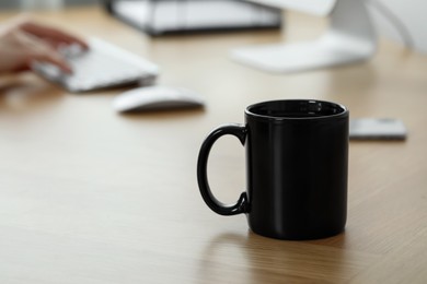 Black ceramic mug on wooden table in office, selective focus. Space for text