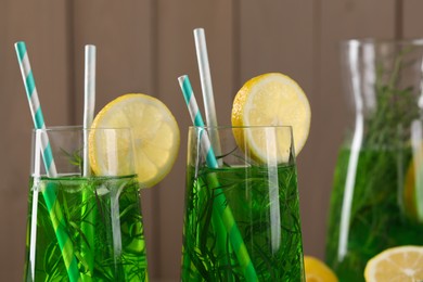 Photo of Glasses of refreshing tarragon drink with lemon slices on wooden background, closeup