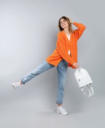 Happy woman with backpack on light grey background