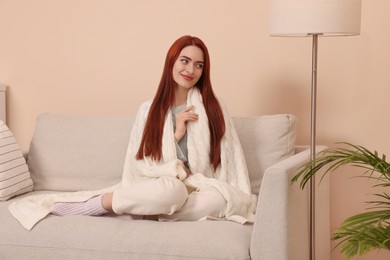 Photo of Beautiful woman with red dyed hair wrapped in white knitted plaid at home