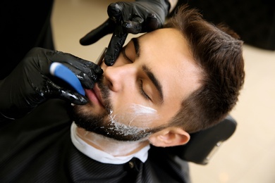 Photo of Professional hairdresser shaving client with straight razor in barbershop