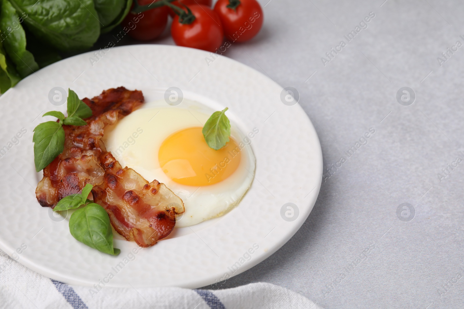 Photo of Fried egg, bacon and basil on light grey table, space for text