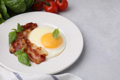 Fried egg, bacon and basil on light grey table, space for text