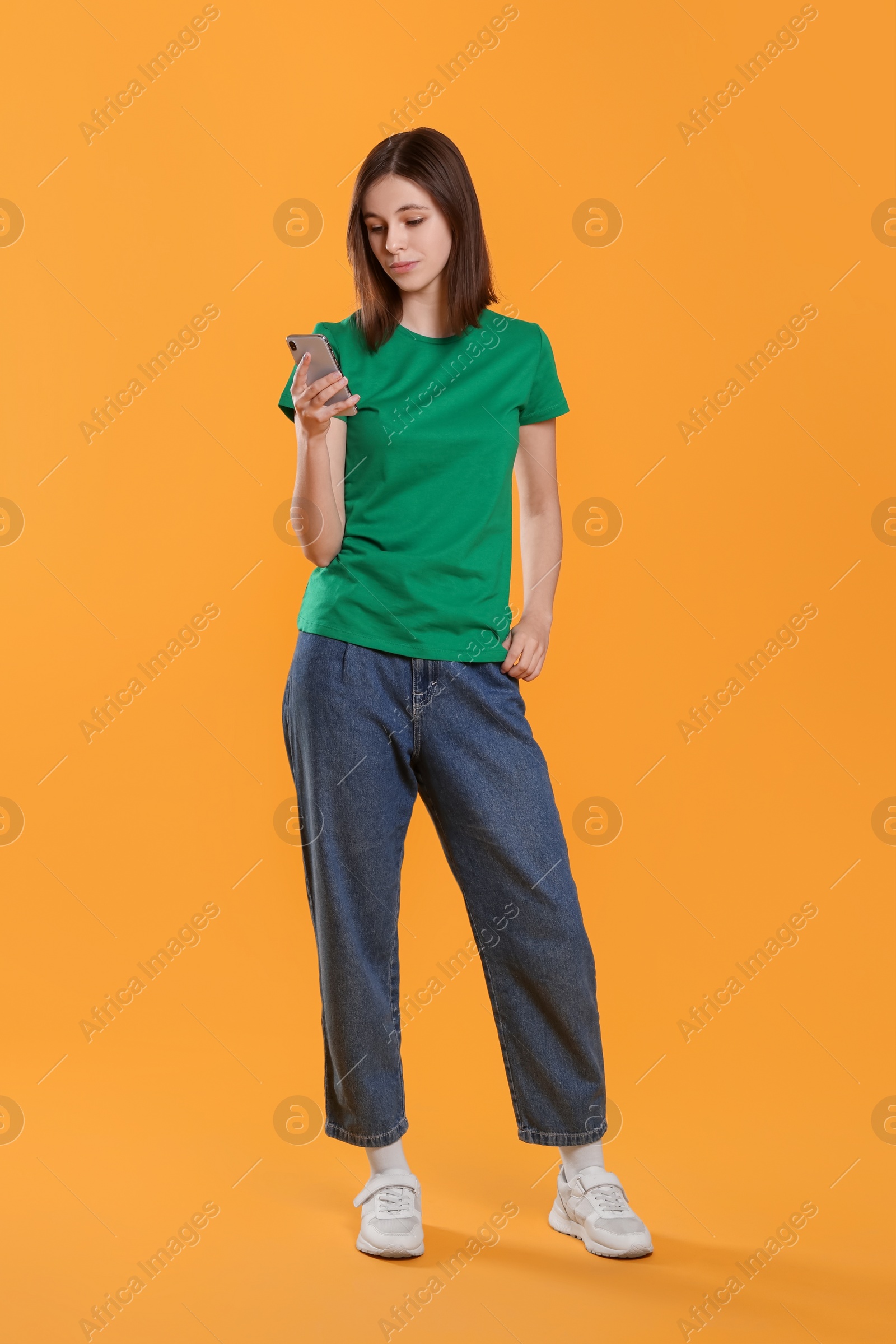 Photo of Teenage girl using smartphone on orange background